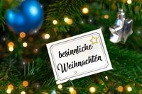 Besinnliche Weihnachten auf einer Karte, umgeben von Weihnachtsbaumzweigen und glitzernder Weihnachtsdekoration.