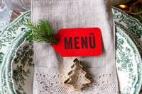 Weihnachtsmenü Tischdekoration mit rotem Menü-Schild, Tannenbaum und Tannenzweig.