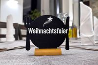 Weihnachtsfeier im Restaurant, Tischdekoration mit Besteck- und Teller-Symbol auf schwarzem Schild.