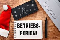 Betriebsferien: Weihnachten, Notizblock, Laptop, Stift und Handy mit Weihnachtsdeko.