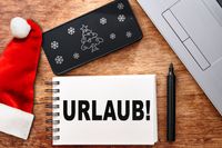 Notiz mit 'URLAUB!' und Weihnachtsmütze. Weihnachtsurlaub-Ankündigung.