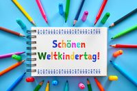 Buntes Notizbuch mit der Aufschrift 'Schönen Weltkindertag!' umgeben von Stiften – Symbol für den internationalen Tag der Kinder.