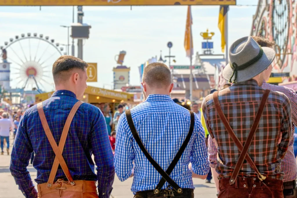Drei männer in traditioneller bayrischer tracht mit lederhosen, die über das oktoberfest schlendern.