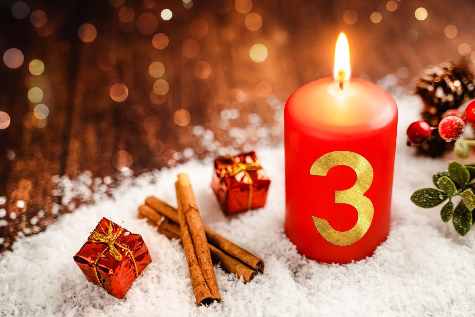 Rote kerze mit der zahl 3, umgeben von zimtstangen und geschenken im schnee als adventsgruß zum 3. Advent.