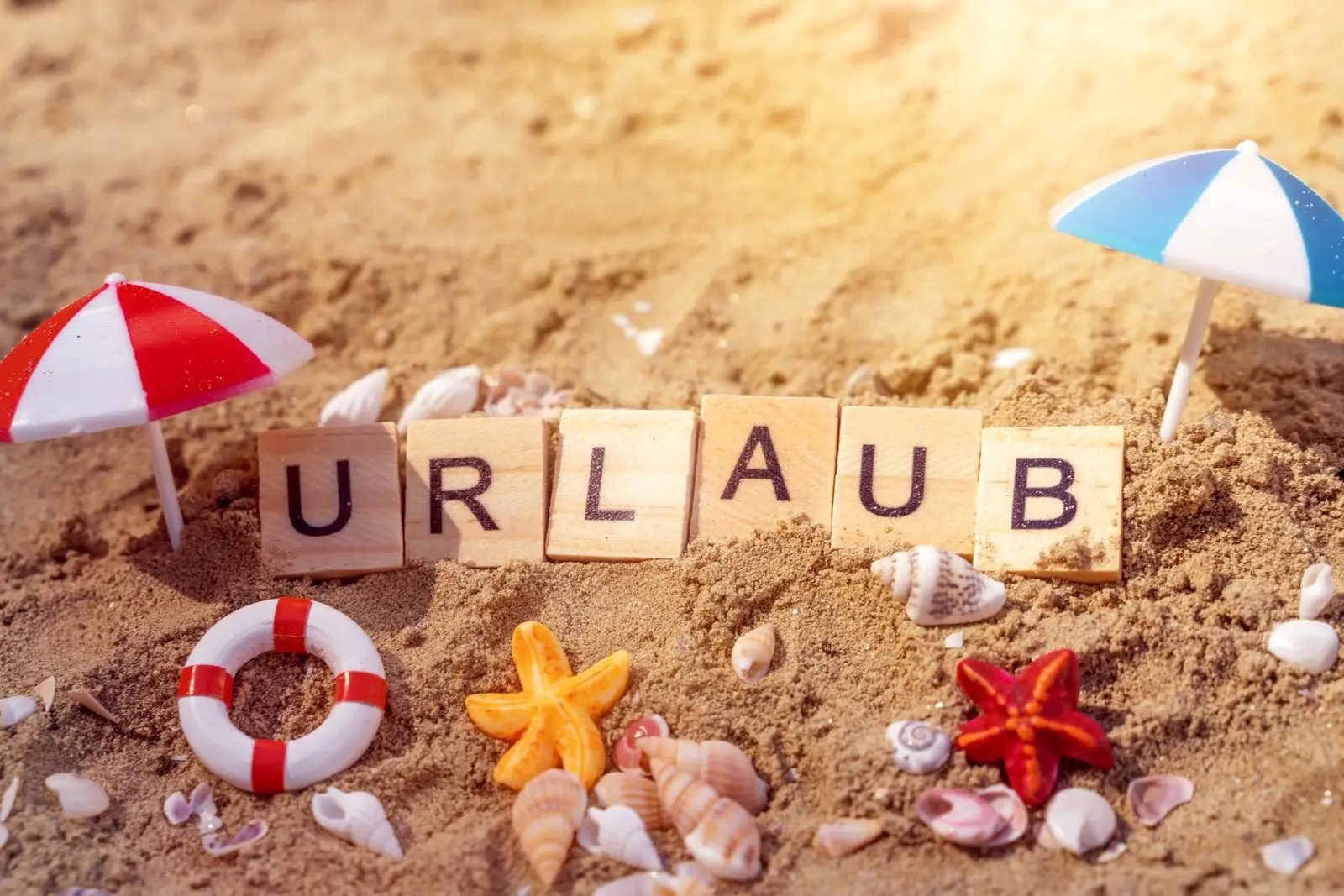 Urlaubsbild mit dem wort ‚urlaub‘ aus holzbuchstaben im sand umgeben von muscheln und sonnenschirmen