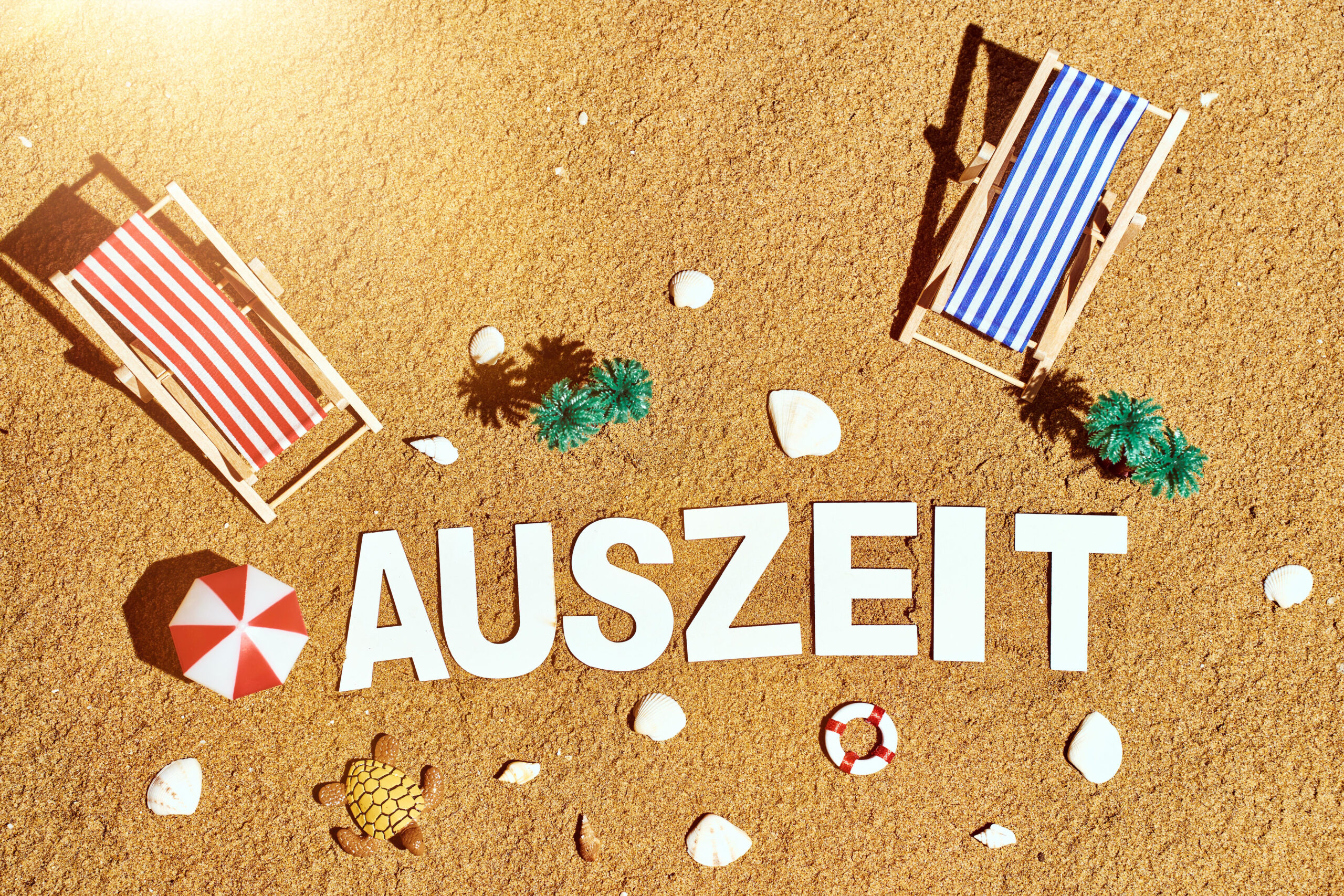 Schriftzug: auszeit, im sand am strand mit sonnenliegen