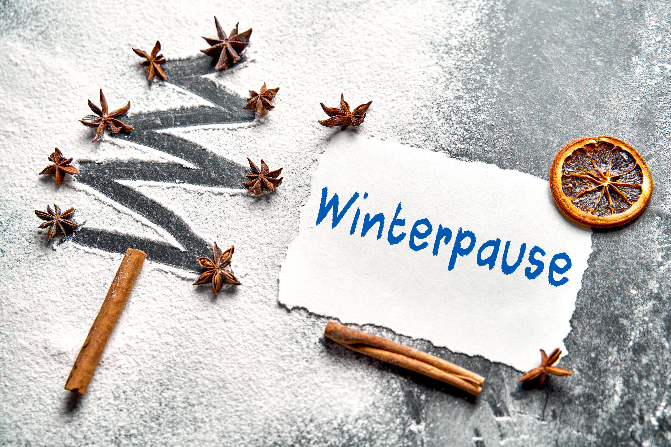 Schriftzug winterpause auf weißem grund mit zimtstangen, sternanis und getrockneter orange